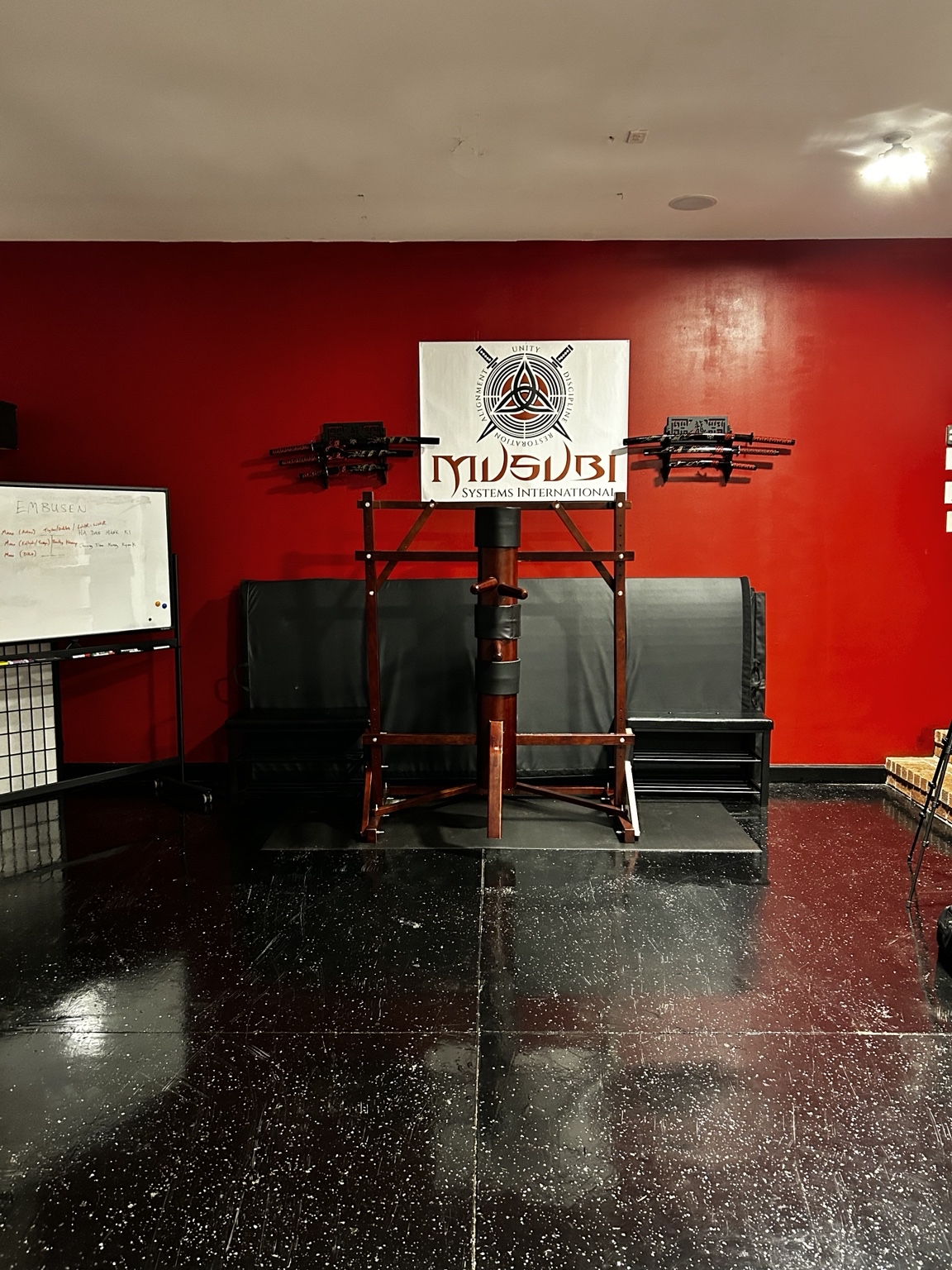 The MUSUBI dojo: red wall, MUSUBI sign, weapons racks and wooden training dummy